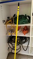 Shelves with multiple extension cords coiled and a long yellow pole or rod in front