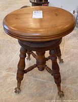 View of round wooden piano stool seat and legs with metal claw feet holding glass balls.