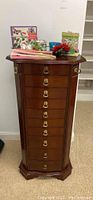 Front view of tall 9-drawer jewelry chest with brass ring pulls and multiple items on top including fans and stationery.