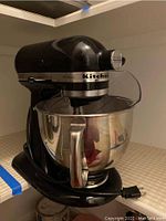 Front-side view of black stand mixer with attached stainless steel bowl and pouring shield