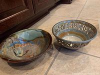 Two pottery bowls and one metal tray on tile floor, showing overall shapes and colors.