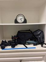 Displayed Nikon AF N6006 camera with lenses, carrying bags, flash attachment, and desk clock on shelf.