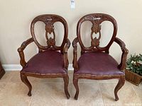 Two carved wood armchairs with burgundy upholstered seats shown side by side, full view of lot