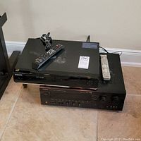 Samsung BD-UP5000 Blu-ray player stacked on top of Yamaha receiver, both black, with remotes on top of Blu-ray player.