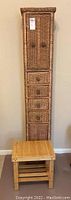 Front view of tall wicker storage unit with closed doors and drawers with bamboo stool in front.