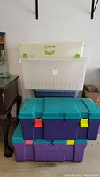 Stacked plastic storage bins and containers of various sizes and colors, showing overall lot contents. Includes purple, teal, clear, and blue bins.