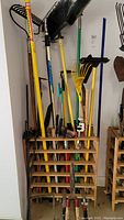 Full view of wooden rack holding an assortment of yard tools including rake, broom, hoe, shears, and umbrella