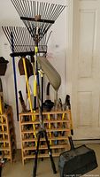 Full view of the wooden tool rack filled with various yard tools including rakes, shovels, loppers, dustpan, machete, and plunger.
