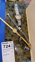 Lot showing three watches and one bracelet on surface, including a gold-tone watch, silver-tone watch, and silver-tone bracelet.