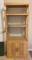 Front view of the wicker shelving unit with three shelves and two doors.