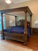 Full view of the wood canopy bed in a bedroom, showing its overall size, design, and the fabric canopy draping.