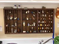 Full view of the wood printer's drawer filled with various miniatures including thimbles, figurines, bottles, and collectibles arranged in cubby compartments.