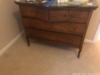 Front view of the wood dresser with four drawers and curved legs, showing drawer handles and wood grain.