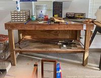 Front view of the wood work table showing the thick wooden tabletop with various items on it (not included), and a lower shelf holding some items.