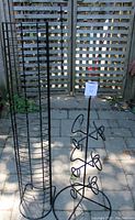 Both black metal racks side by side outdoors on patio tiles with lattice fence background.