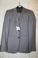 Light grey Calvin Klein suit jacket hanging on a hanger showcasing front view with two buttons and flap pockets.