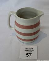 Front angle view showing the full shape, handle, spout, and pink stripe design on the creamer