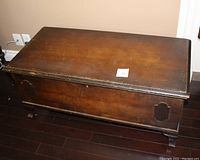 Overall view of cedar chest showing rectangular shape, dark brown wood finish, and carved legs. Visible scratches on surface.