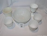 Group photo of six milk glass items: three stemmed glasses, one goblet, fluted vase, and large bowl