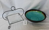 Clear square glass plate on black wrought iron stand next to large round pottery bowl with turquoise and brown glaze