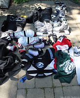 Wide view of the complete lot showing skates, pads, gloves, pants, and jerseys arranged outdoors on patio stones.