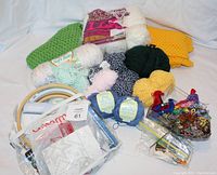 Wide view of the wool yarn in many colors, completed green shawl and yellow runner, embroidery hoops, mini quilt kit, crochet hook, and assorted needles and accessories.