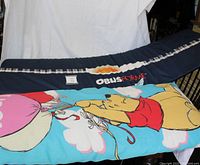 Image showing both pillows side by side: the ObusForm full body support pillow in dark blue with plaid stripe and logo, and the kids Winnie the Pooh pillow in bright blue with printed Pooh design.