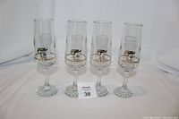 Front view of four clear glass champagne flutes with 1988 Calgary Olympic gold emblems, arranged in a row.