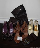 Photo displaying three pairs of women's shoes: brown strappy sandals, black and plum peep-toe heels with bow detail, and cream pointed-toe heels alongside a pair of black leather boots lying horizontally.