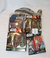 Four Star Wars figures and one ship toy in original packaging arranged on flat surface. Clear plastic windows on packaging show figures and accessories clearly. Figures include Chewbacca, Leia, and others.