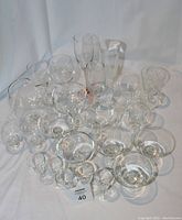 Full set of 24 assorted stemmed glassware on white cloth background including brandy snifter, champagne coupes, flutes, liqueur and wine glasses.