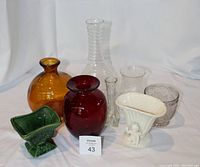 Group photo of eight vases showing variety in glass colors and styles: amber, red, clear, green, white with cherub.