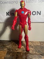 Front view of Iron Man action figure standing upright on a table with visible detailed red and gold armor and blue arc reactor on chest.