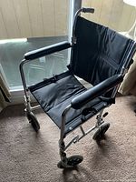 Full view of the AMG medical transport chair from an angle, showing padded armrests, black fabric seat and backrest, and chrome frame.