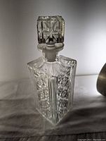 Front view of clear crystal decanter with square stopper showing intricate cut detail.