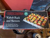 Box showing product name 'Charcoal Companion Kabob Rack and Skewers' and product specifications including six skewers, 14 inches long, easy turning, food won't stick, grill rack folds for storage.