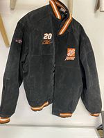 Front view of large black jacket with Home Depot Racing logo, number 20 embroidery, and striped collar and cuffs.