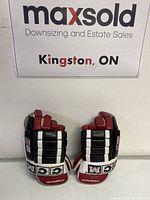 Pair of youth hockey gloves by CCM, branded on cuff with black, white and red color scheme, viewed from back of hand side.