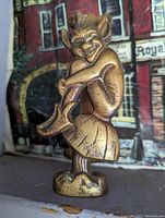 Close-up photo of brass pixie door knocker, showing the detailed figure with crossed legs and smiling face.