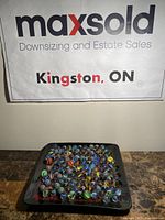 Photo showing the full lot of marbles on a dark surface with a MaxSold Kingston ON sign behind.
