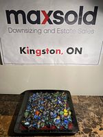 Photo showing a large number of assorted glass marbles on a black square dish (not included). Marbles vary in color and pattern, including blues, greens, oranges, yellows, blacks, and clear with multicolored swirls.