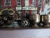 Side view of motorcycle sculpture showing detailed engine, wheels, and kickstand with Royal Tavern backdrop