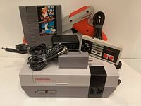 Photo displaying the NES console with Mario Bros./Duck Hunt game cartridge inserted, standard controller, Zapper light gun, power adapter, and RF switch cable arranged behind the console.