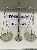 Front view of the complete silver-coloured metal scales of justice showing the central stand, horizontal beam with balance pans suspended by chains, and weighted base.