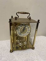 Vintage brass anniversary mantel clock approx. 10 inches tall, with glass case and Roman numeral dial.