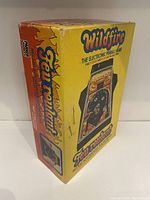 Photo of the Wildfire mini arcade electronic pinball game original packaging. Shows the yellow and red box with flame motifs and the game artwork with pinball table