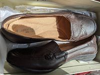 Top view of the pair of women's dark brown leather Naturalizer shoes inside the box showing cushioned insoles and round toe design with stitching detail.