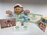 Cabbage Patch Kid doll with accompanying birth certificate and memorabilia laid out flat.