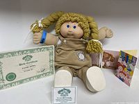 Full shot of doll sitting with birth certificate and cards near it