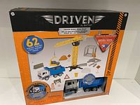 Front view of the boxed toy showing the set's contents including the dump truck, crane, construction signs, and mention of 62 pieces.